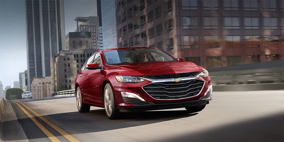 Vue avant de la Chevrolet Malibu 2023 en teinte rouge éclatant en mouvement au centre-ville.