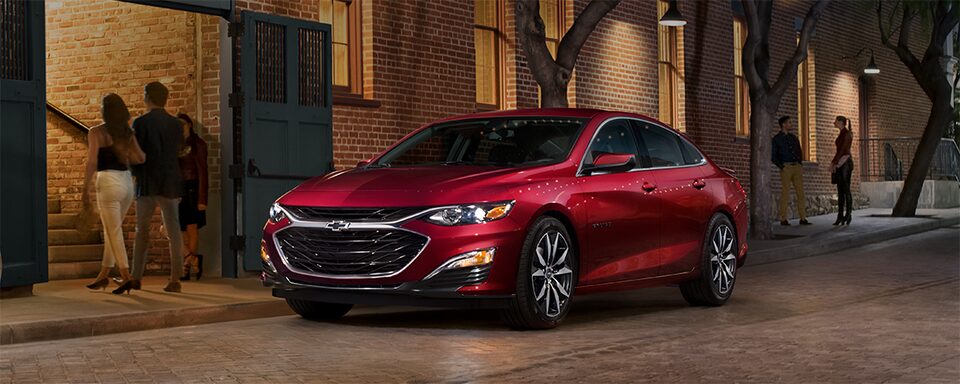 Vue panoramique de la Chevrolet Malibu 2023 en teinte rouge éclatant dans la ville, la nuit.