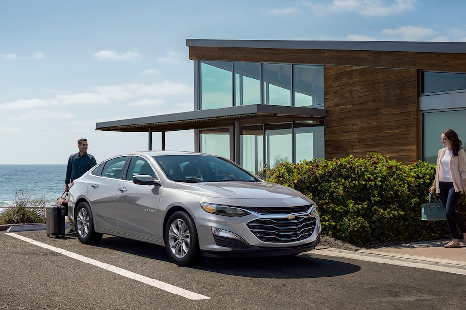 Une personne ouvre le coffre de sa Chevrolet Malibu 2024 dans le terrain de stationnement d’un hôtel.