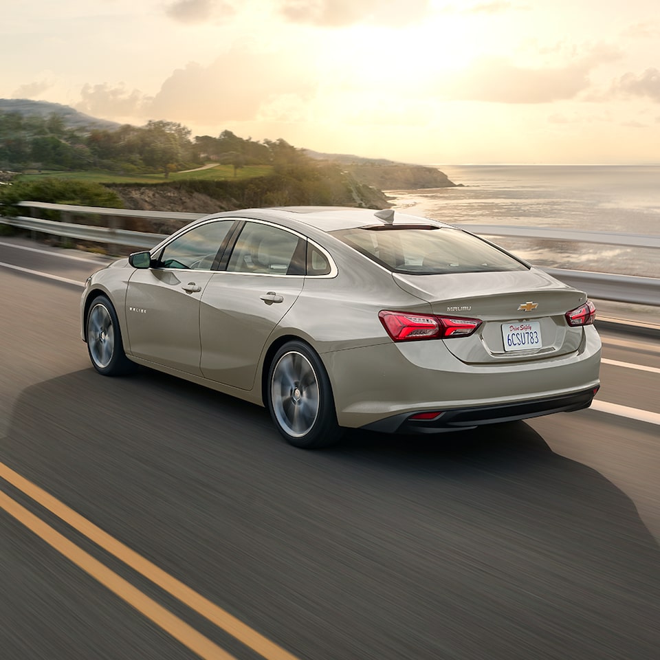 La Chevrolet Malibu 2024 en gris minéral métallisé en mouvement au bord de la mer ensoleillée.