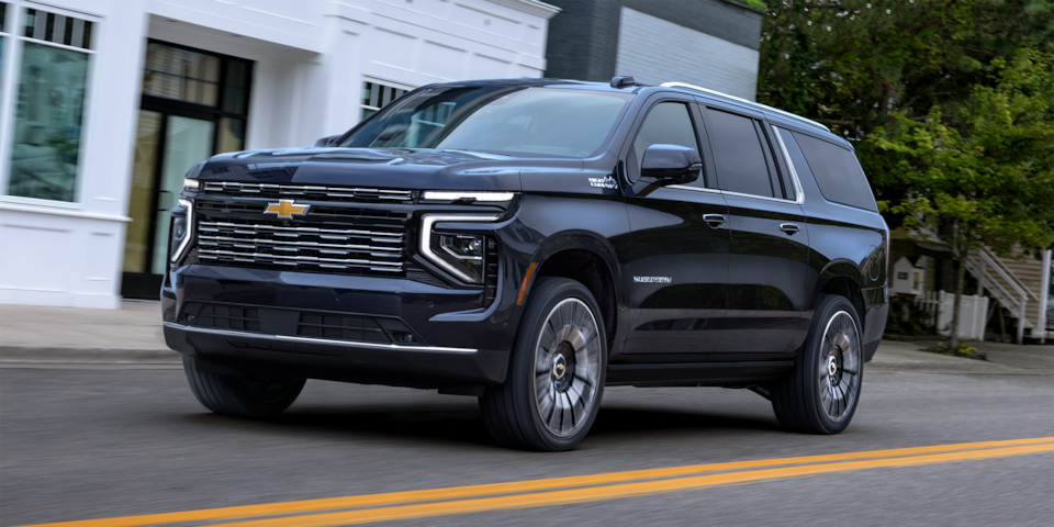 Front three-quarters view of the 2025 Chevrolet Suburban driving by a house.