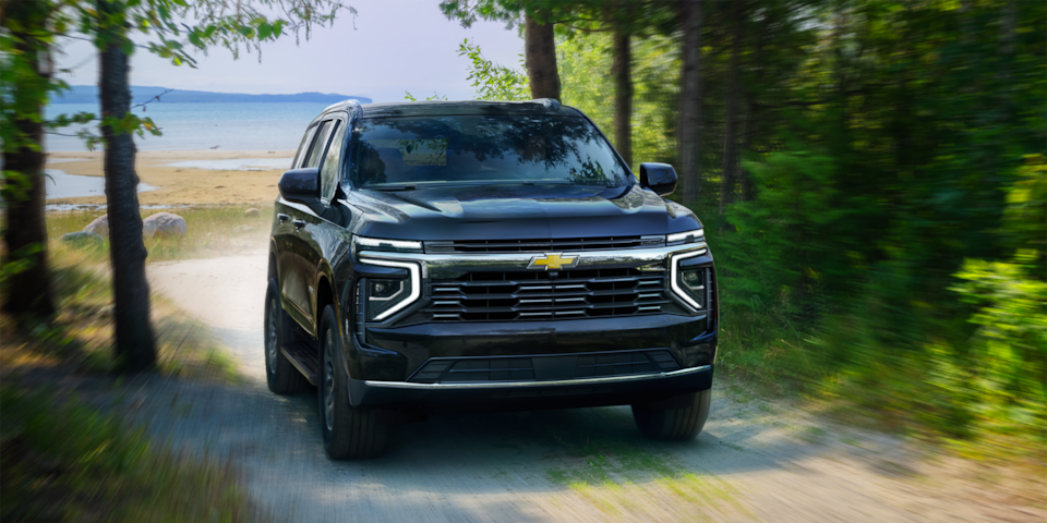 Front three-quarters view of the 2025 Chevrolet Tahoe driving down a gravel path by trees.