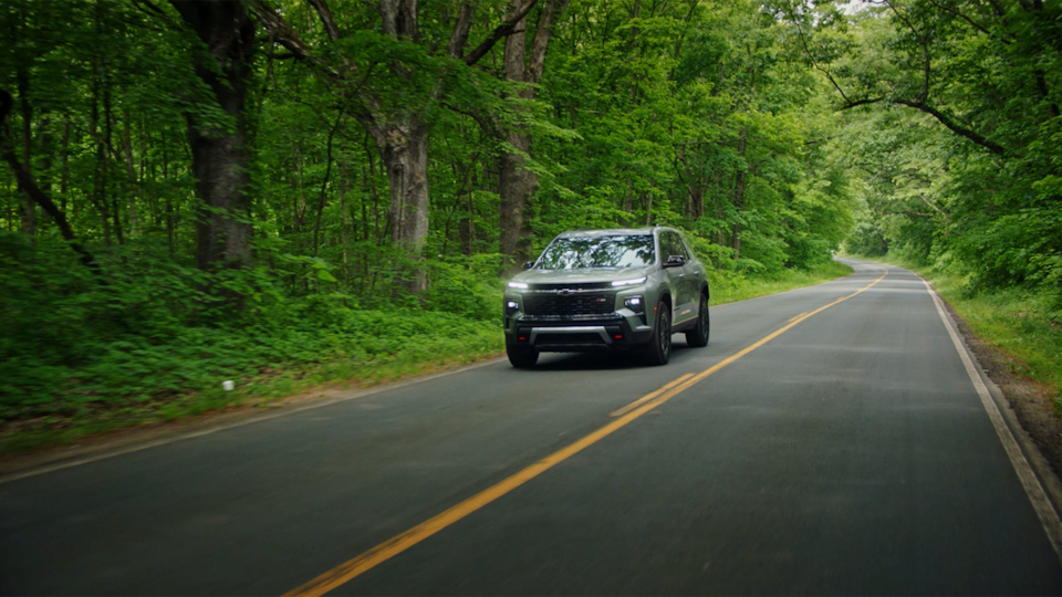 Front-side view of the 2025 Chevrolet Traverse SUV driving on a tree-lined road.