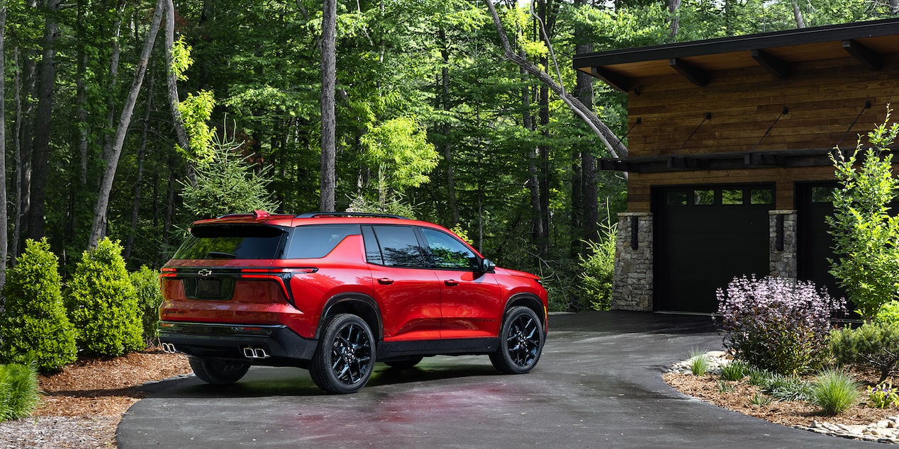 Vue latérale arrière du VUS Chevrolet Traverse 2025 stationné devant une maison en bois.