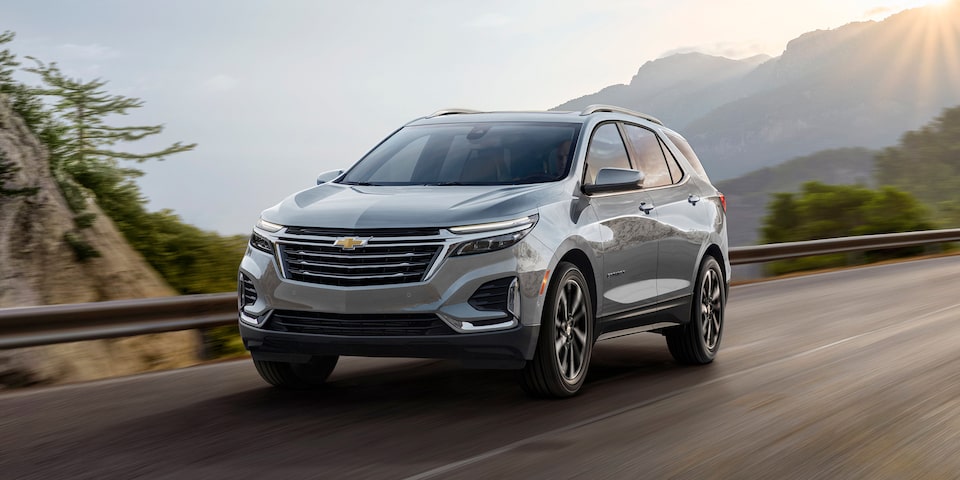 Le Chevrolet Equinox 2024 en mouvement sur une belle route montagneuse avec le soleil à l’horizon.