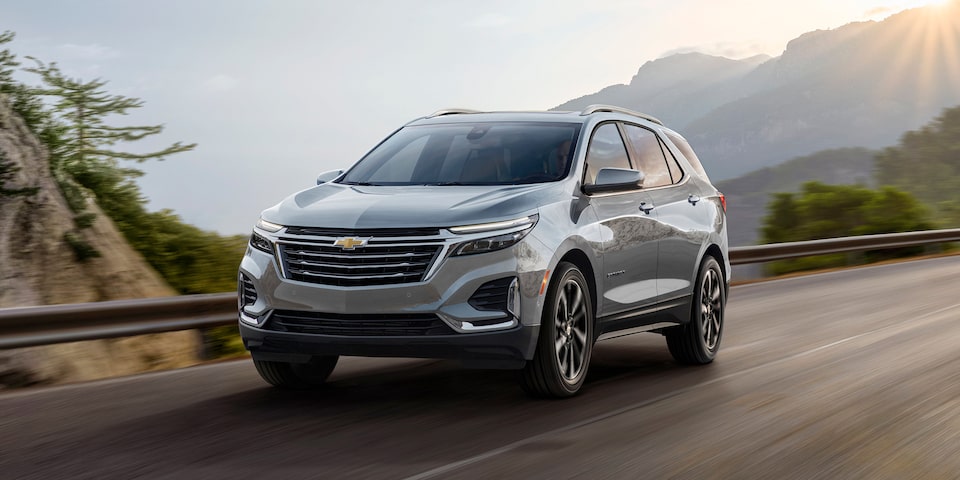 The 2024 Chevrolet Equinox driving on a beautiful mountain road with the sun on the horizon.