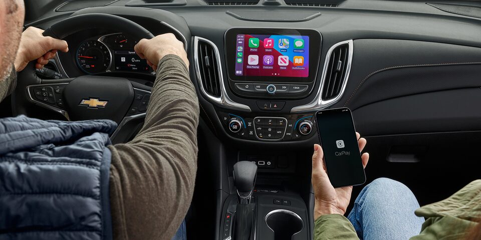 A passenger of the 2024 Chevrolet Equinox uses her phone to sync with Apple CarPlay on the infotainment system.