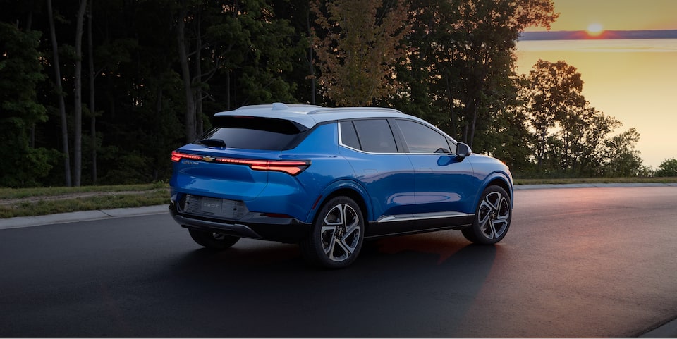 Un VÉ Chevrolet sur une route bordée d’arbres au coucher du soleil.