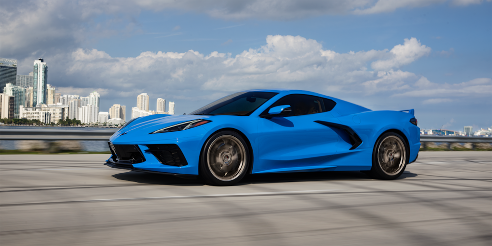 Chevrolet Corvette Stingray 2024 en bleu rapide sur une autoroute avec un paysage urbain en arrière-plan.