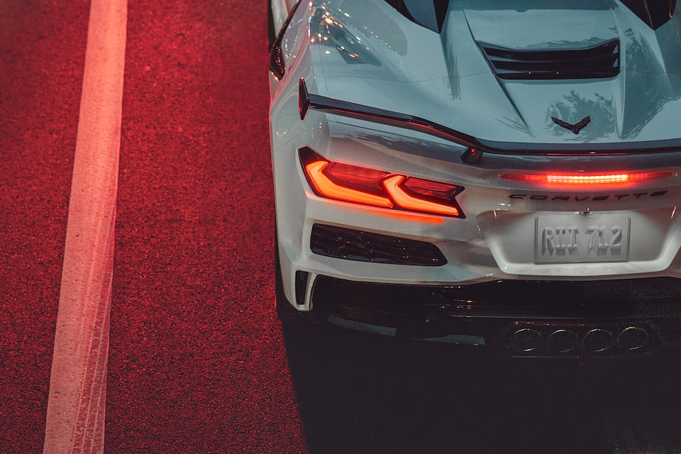 The sleek rear end design of the Corvette Z06 basking under a bright red traffic light.
