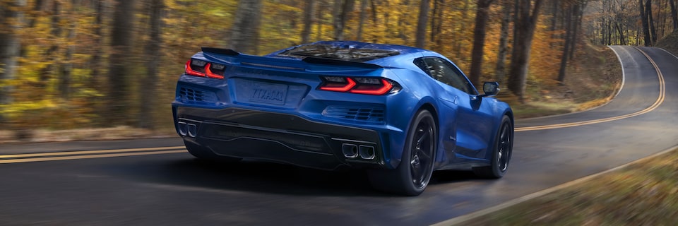 Rear View of a Blue Chevrolet Corvette E-Ray Driving Down the Road Surrounded by Trees.