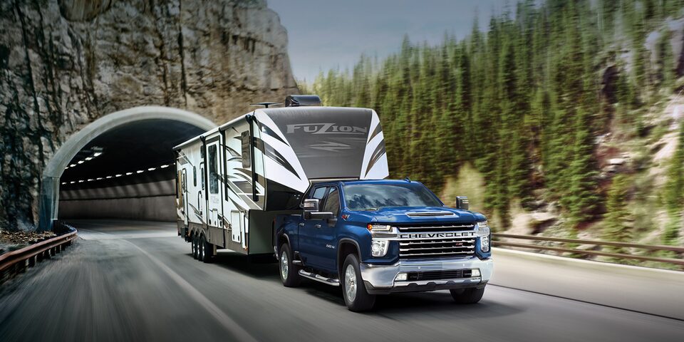Chevrolet Silverado HD 2023 qui remorque un véhicule récréatif sur une route de montagne.