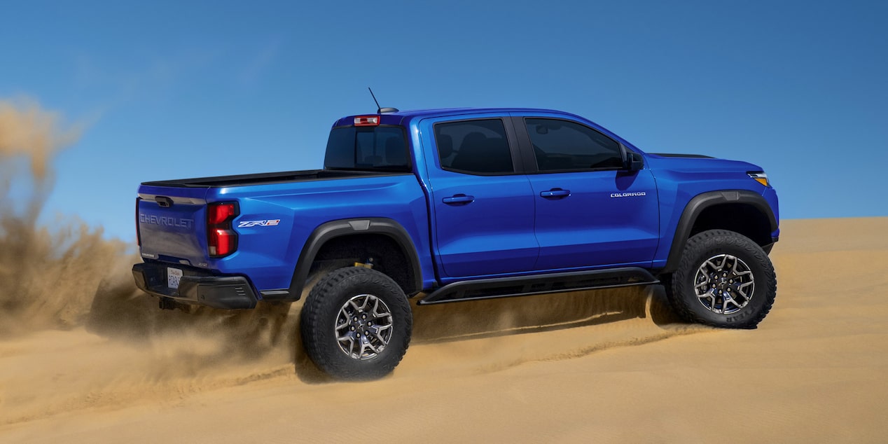 Vue latérale du Chevrolet Colorado 2025 montant une dune dans le désert.