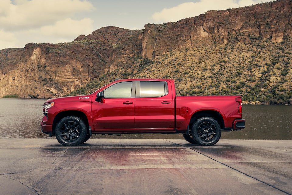 Side-view of a red-colored 2024 Chevrolet Silverado 1500 on a smooth terrain.