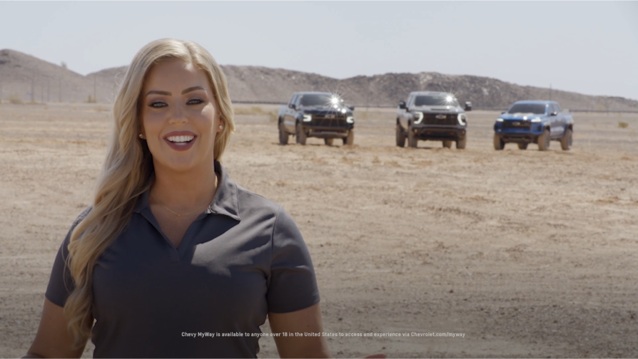 A person standing several meters away from three Chevrolet ZR2 Off-Road Trucks parked in a dusty terrain.