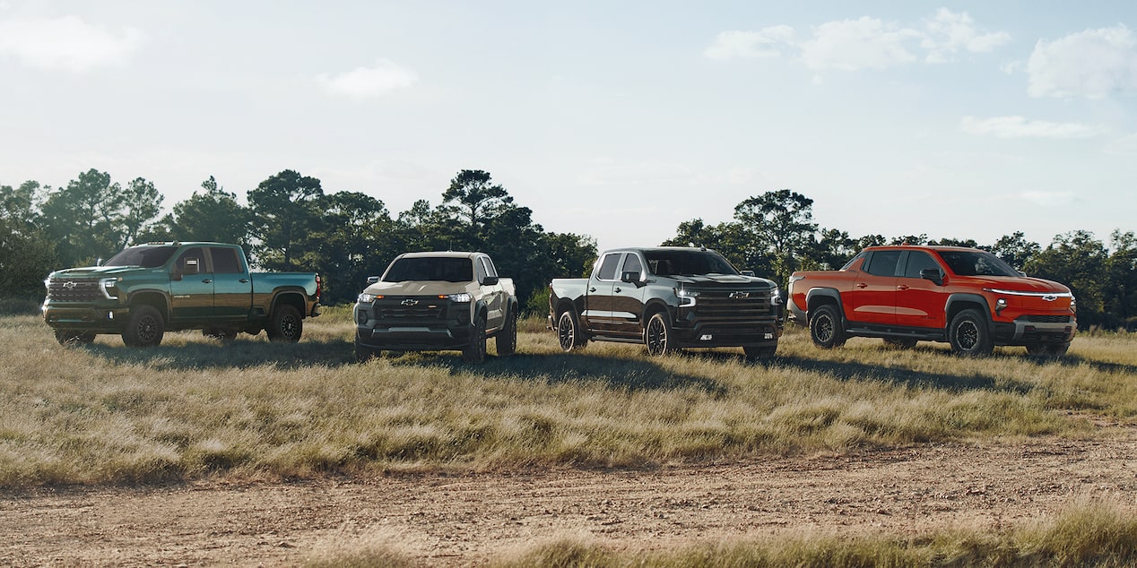 Four Chevrolet Pickup Trucks Including a Silverado ZR2, Silverado HD ZR2, and Colorado ZR2 Parked on a Dirt Road in a Grassy Field.