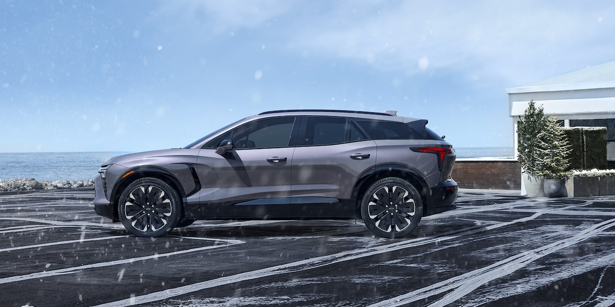 Vue latérale du Chevrolet Blazer EV stationné seul dans une entrée pendant qu’il neige.