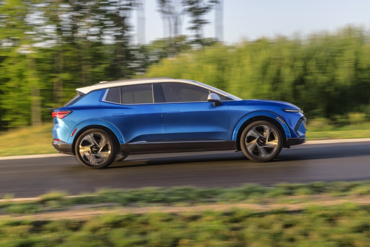 Side view of a Chevrolet Electric SUV driving on a tree-lined road.