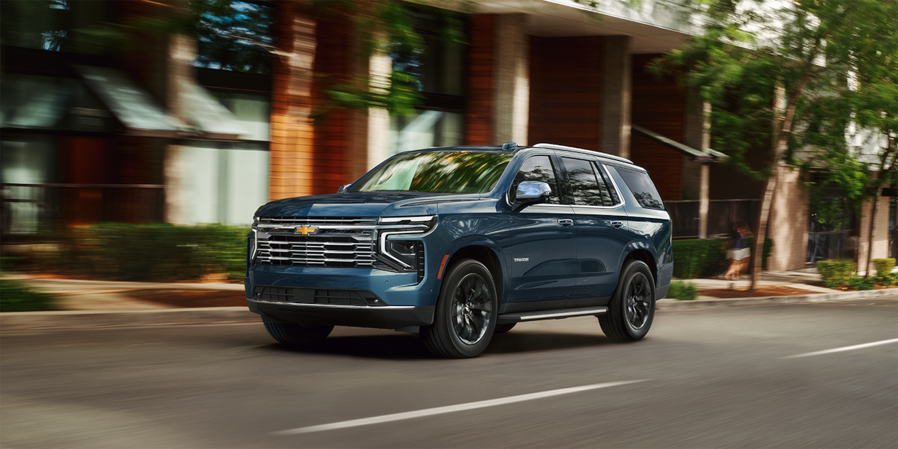 Front three-quarter view of a Chevrolet Suburban large SUV driving fast in the city.