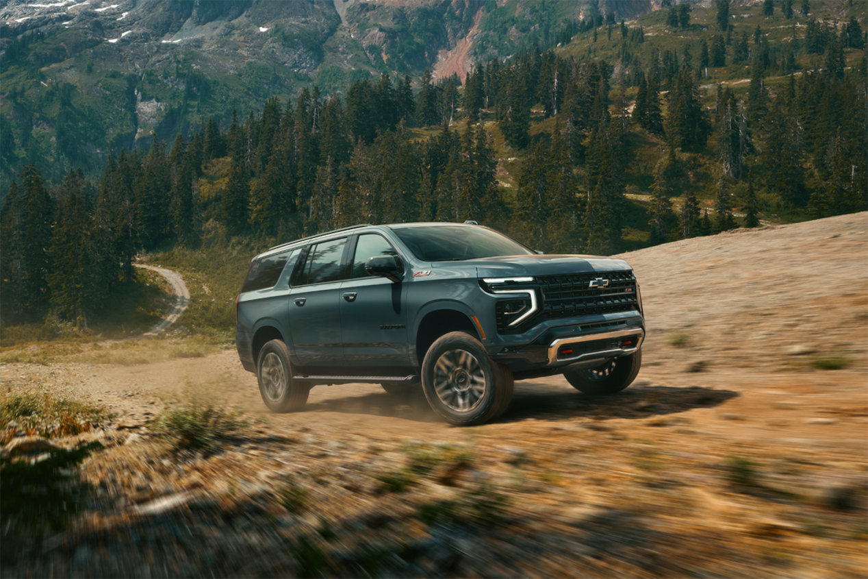 Front three-quarter view of a Chevrolet Suburban large SUV driving on a dusty terrain.