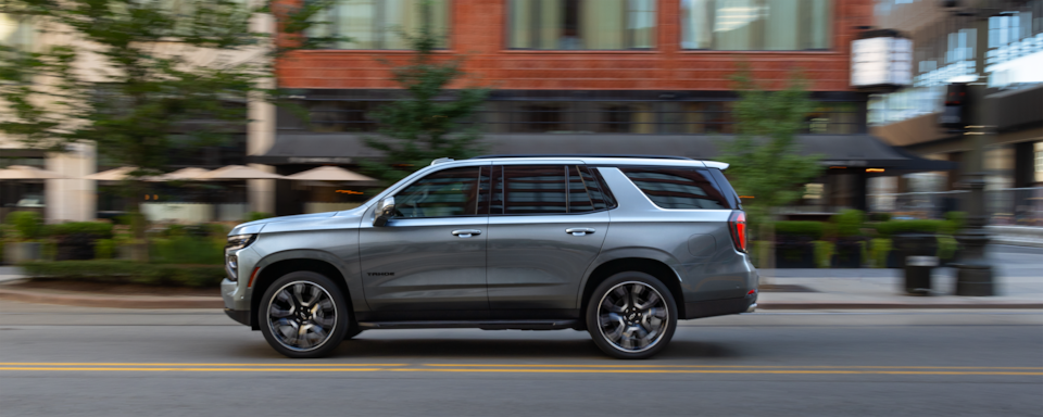 Side view of the 2025 Chevrolet Tahoe SUV driving on a road in the city.