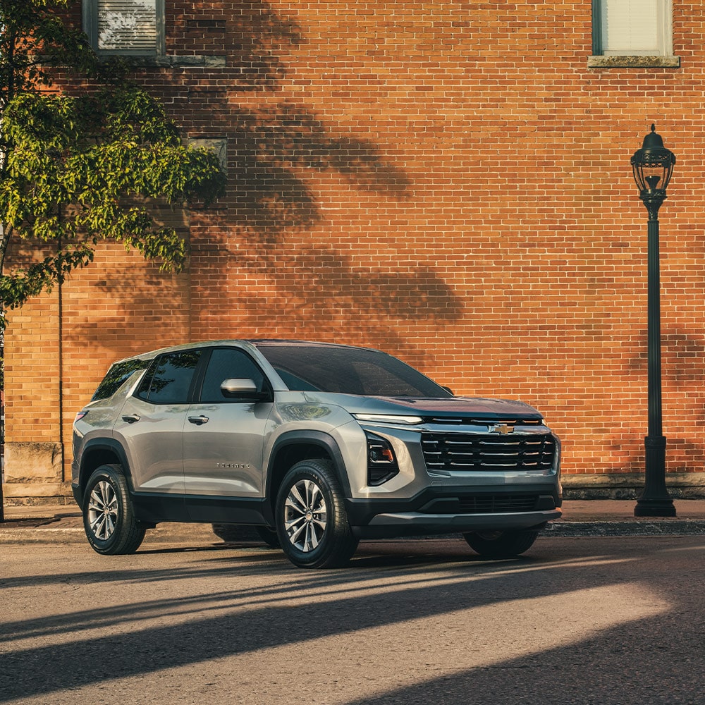 Front-side view of the 2026 Equinox driving past a red brick wall.