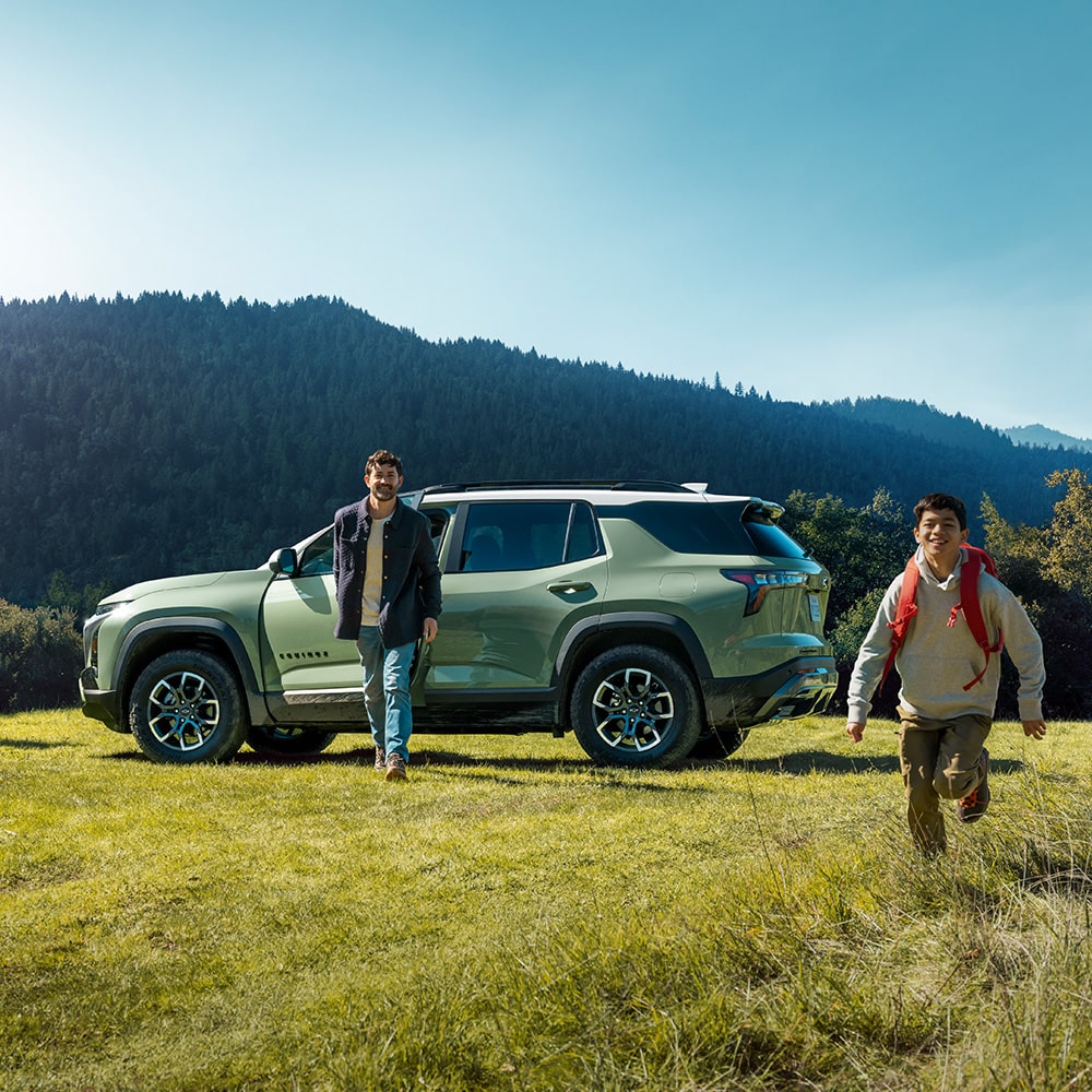 Two people exiting from the 2026 Chevrolet Equinox parked on a grassy field.