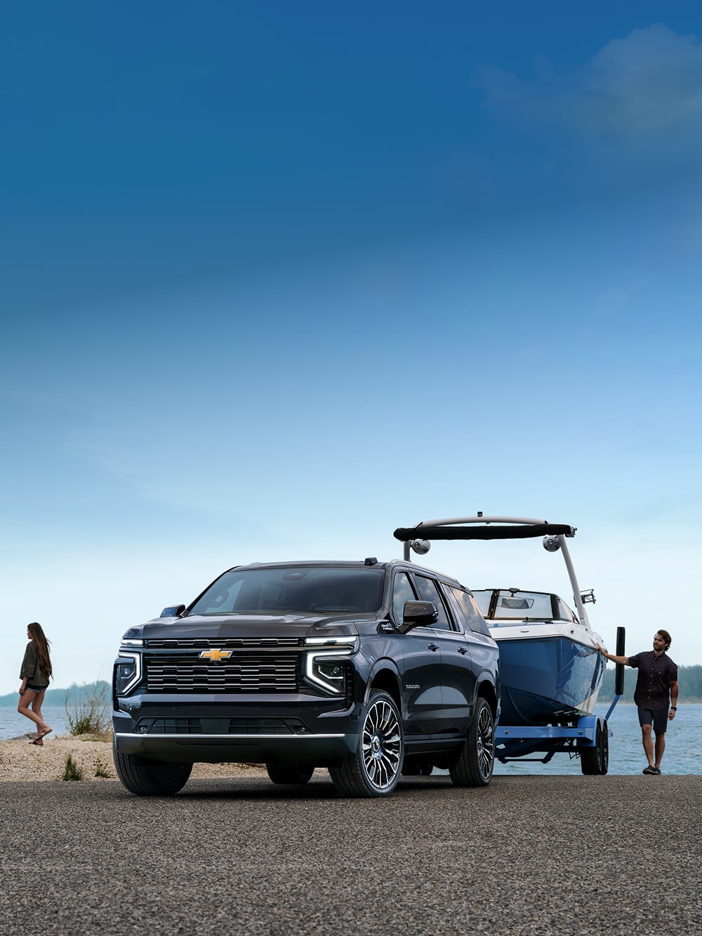 Un Chevrolet Suburban 2026 qui remorque un bateau devant un lac, avec des gens qui marchent à côté.