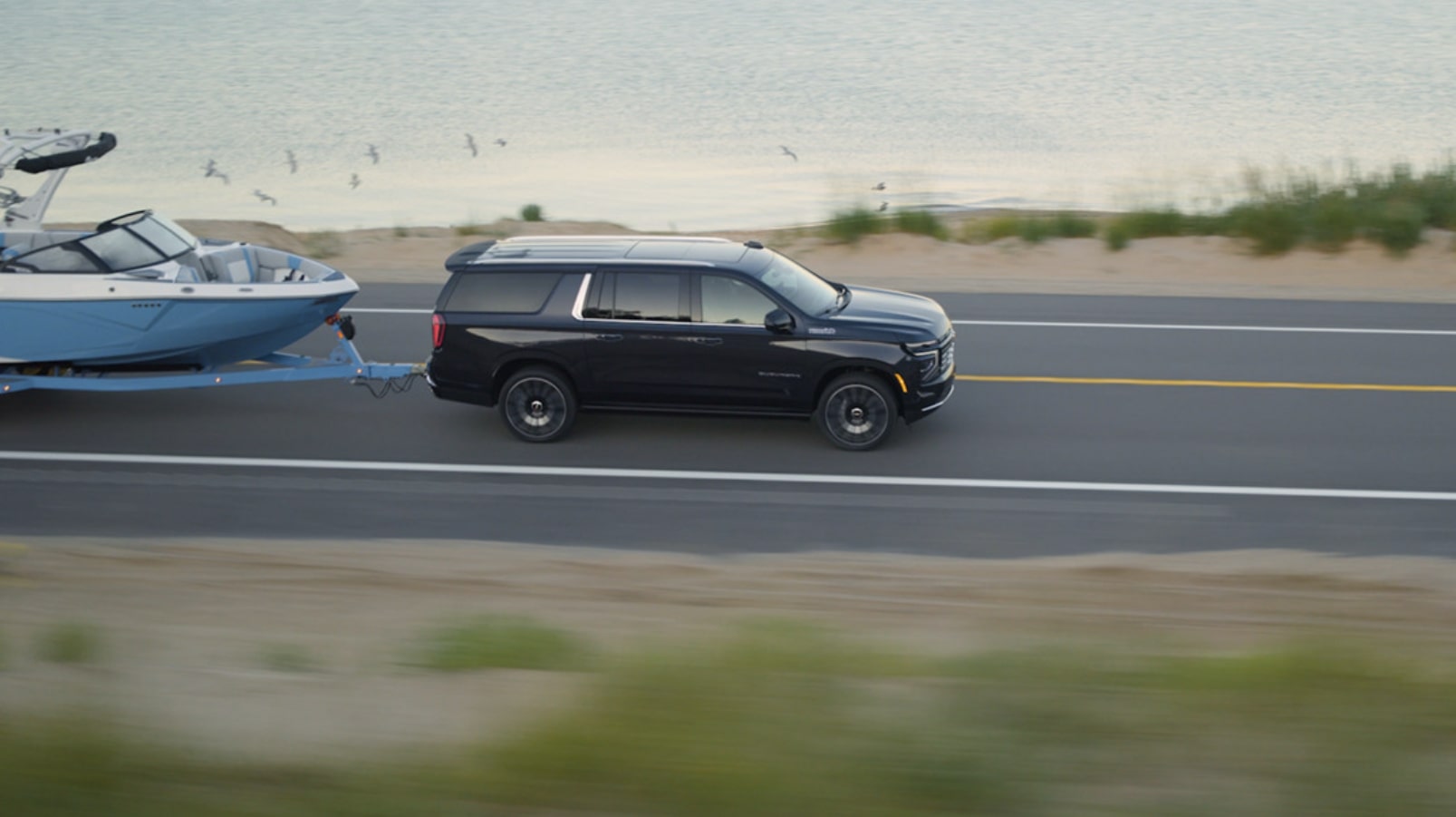 Bird's Eye View of a 2026 Chevrolet Suburban Towing a Boat Near a Lake.