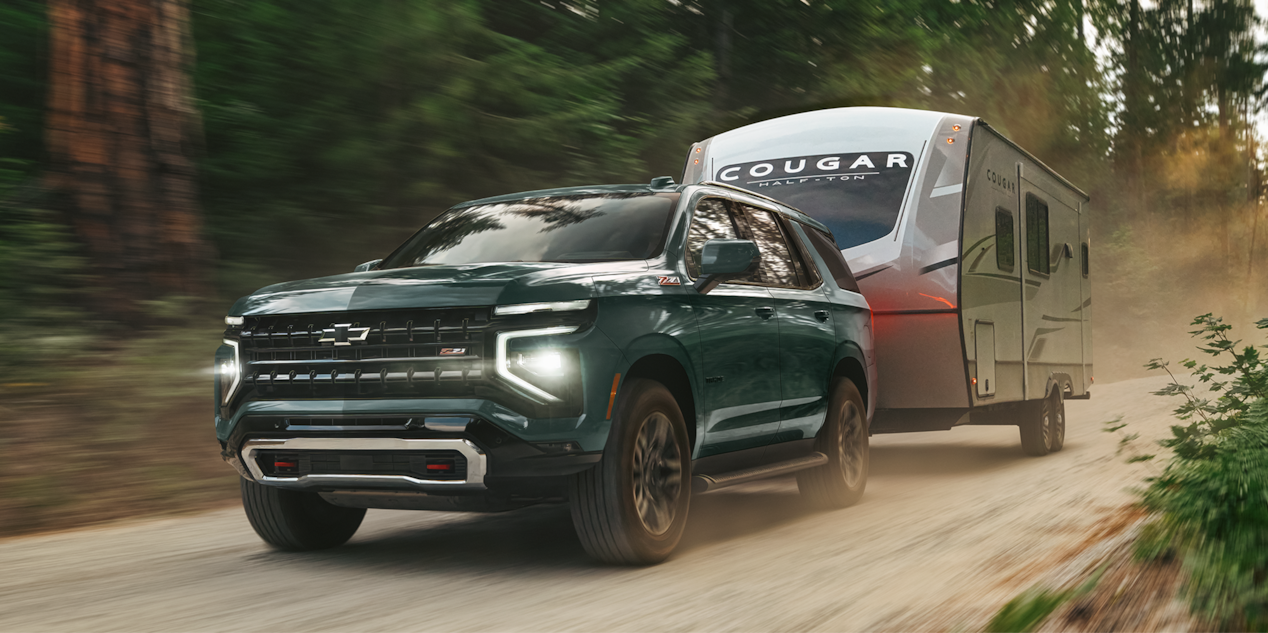 A 2026 Chevrolet Tahoe Hauling a Trailer on a Dirt Road Through the Woods.
