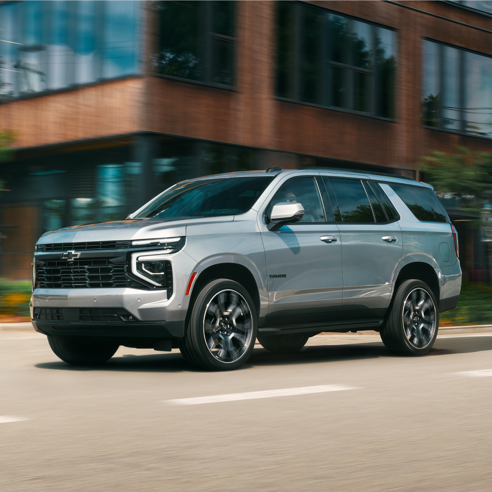 Vue latérale du VUS Chevrolet Tahoe 2026 qui passe devant un complexe d’appartements moderne.
