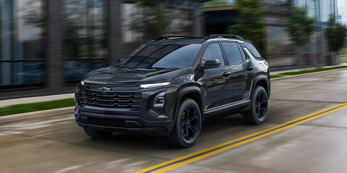 Three-quarter View of a Black Chevrolet Equinox Driving Down a Building Lined with Windows. 
