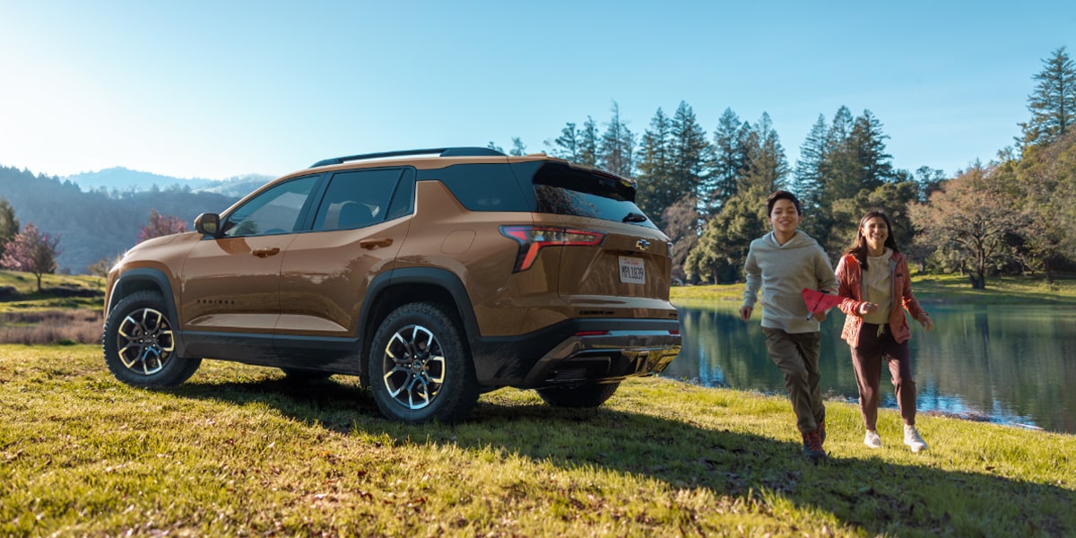 The Sun Shining Down on the Chevrolet Equinox Parked Outside of a Camping Spot While a Man Takes a Picture of Two Campers
