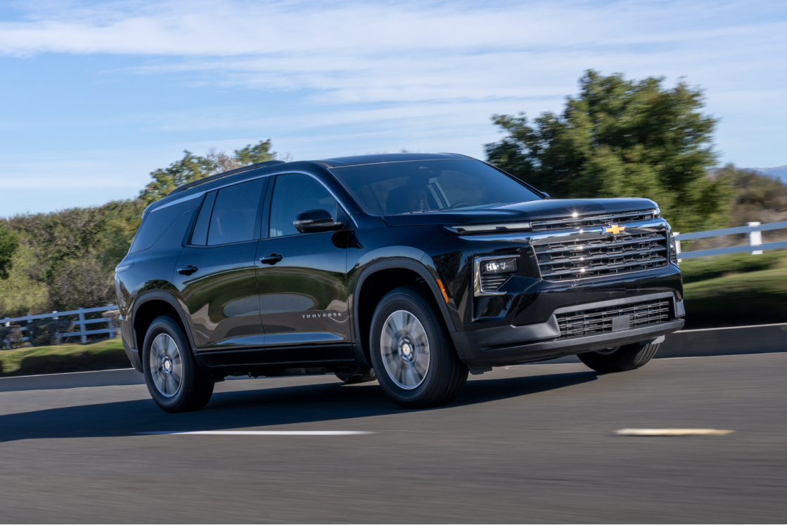 Vue latérale de la Chevrolet Traverse 2027 roulant sur une route bordée d’arbres.
