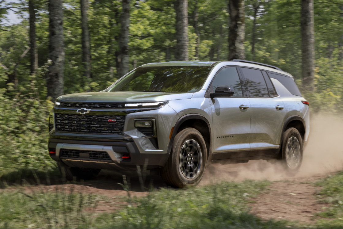 Vue latérale de la Chevrolet Traverse 2027 traversant une route forestière.