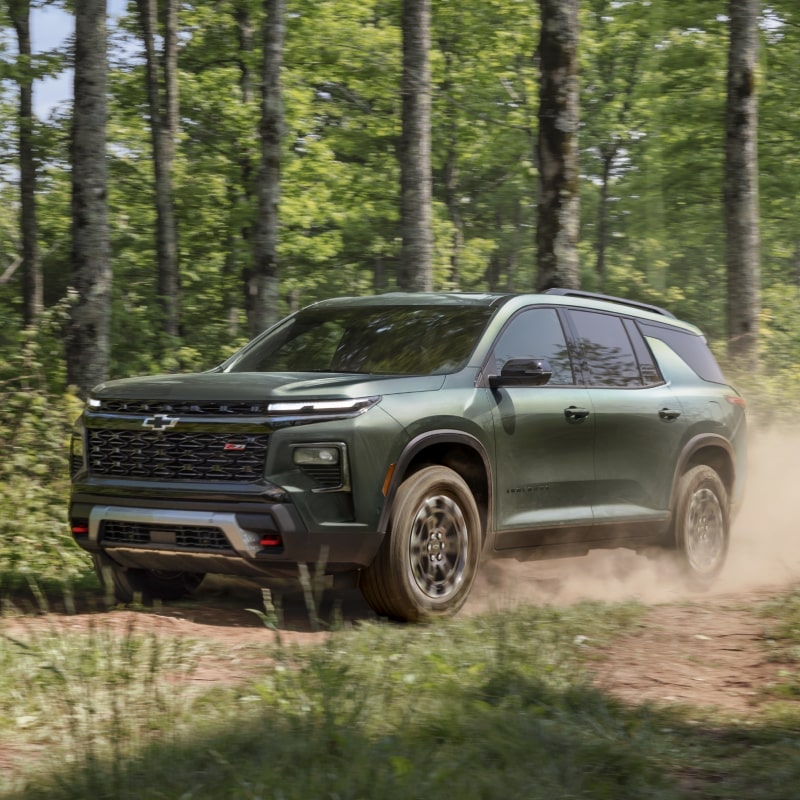 Vue latérale de la Chevrolet Traverse 2027 traversant une route forestière.