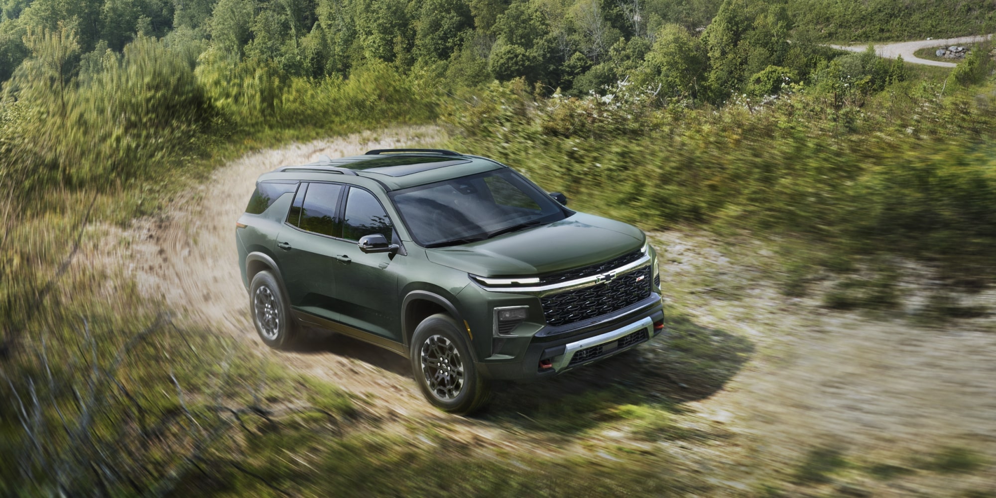 Chevrolet Traverse 2027 roulant sur un terrain accidenté bordé d’arbres.