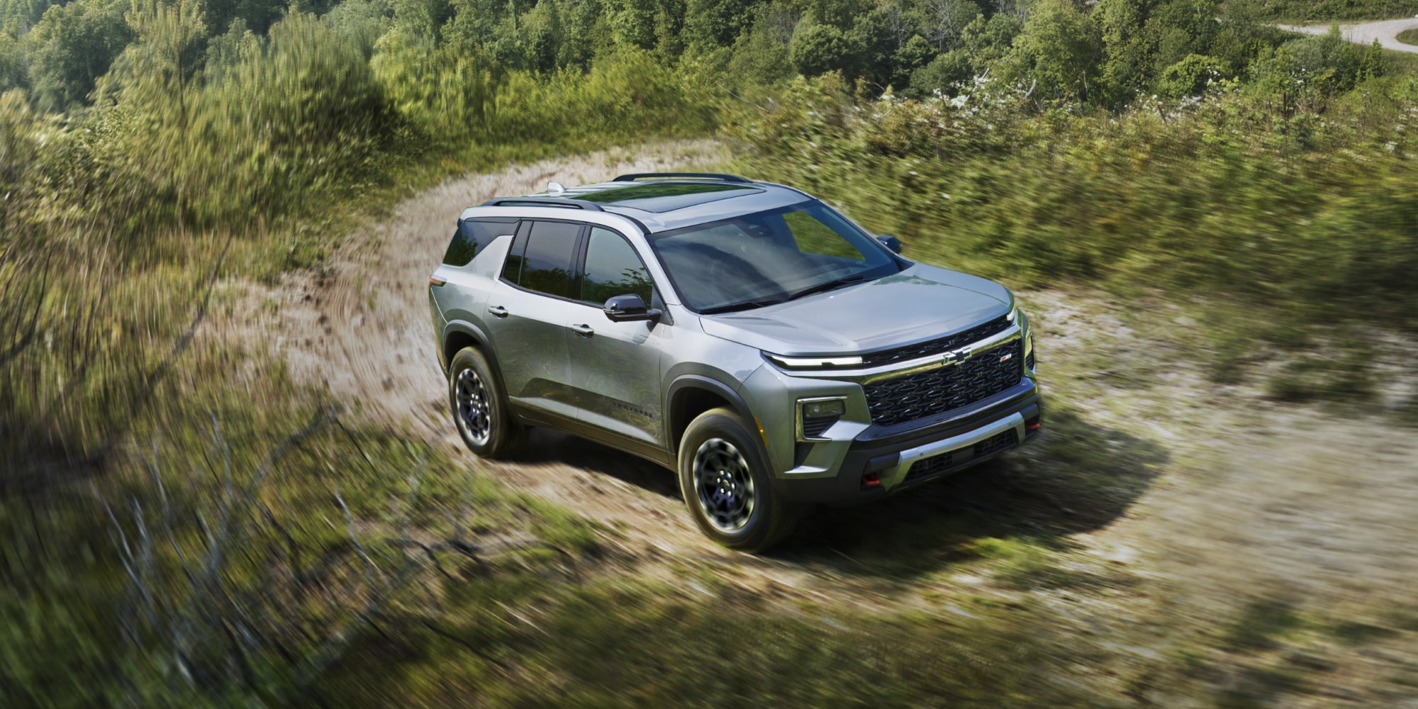 Chevrolet Traverse 2027 roulant sur un terrain accidenté bordé d’arbres.