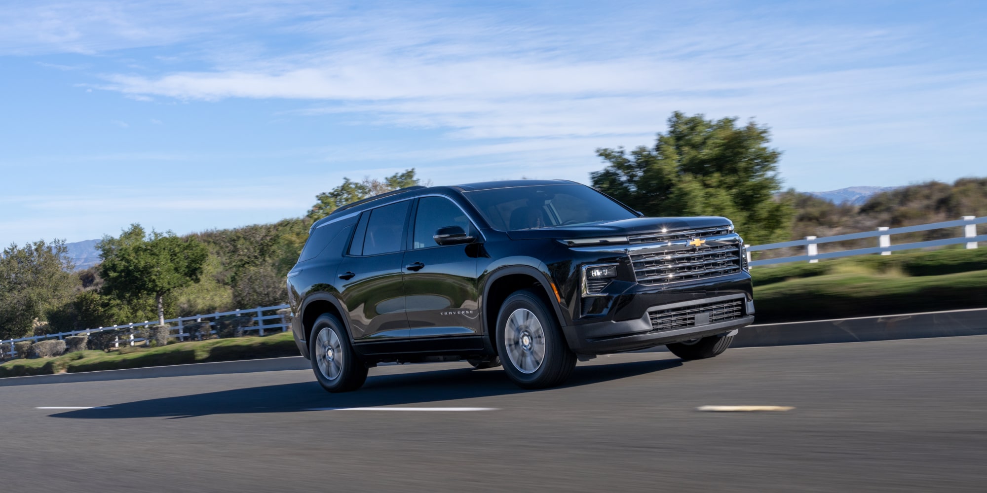 Chevrolet Traverse 2027 conduisant seul sur une route bordée d’arbres.