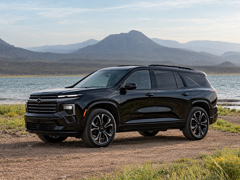 Side view of the 2027 Chevrolet Traverse parked on a dirt path beside a lake.