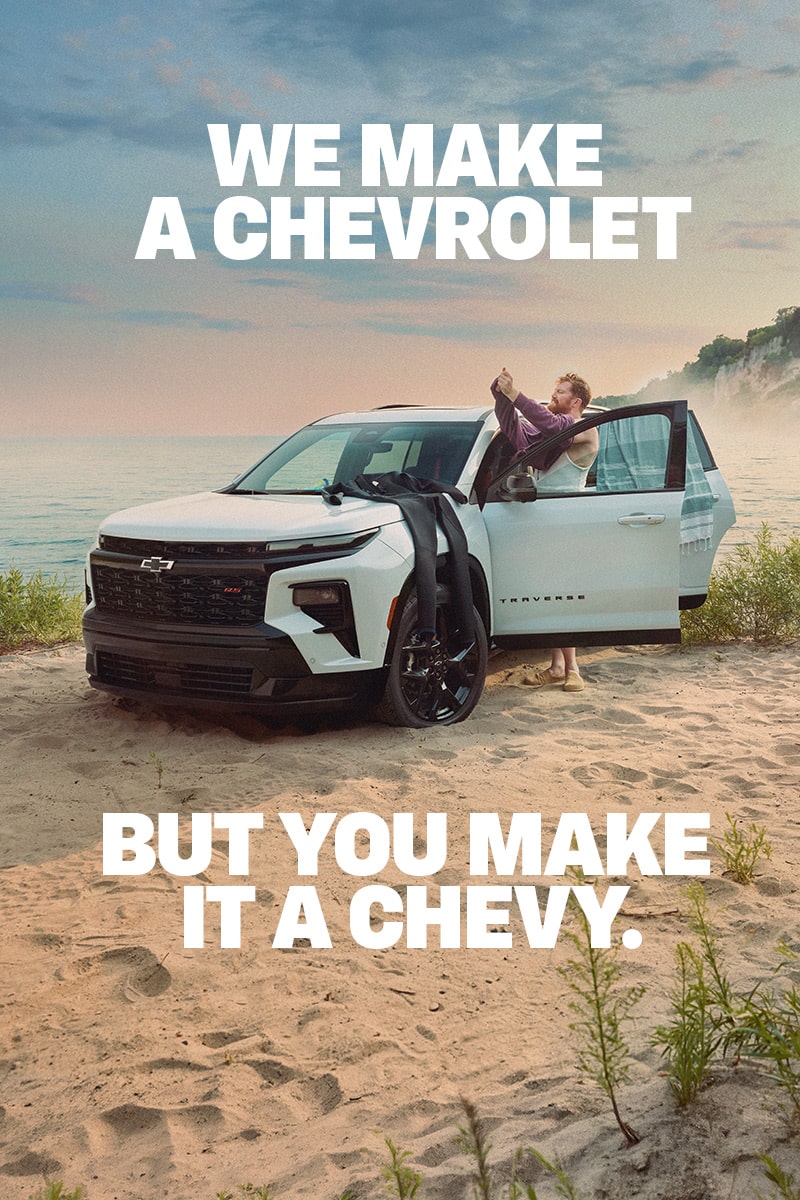 Side view of the 2027 Chevrolet Traverse parked on a dirt path beside a lake.