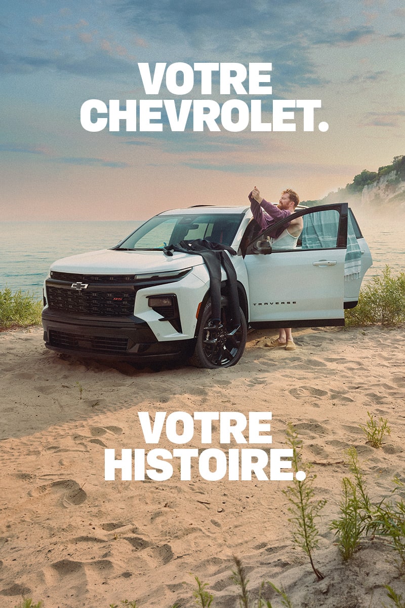 Vue latérale de la Chevrolet Traverse 2027 stationnée sur un sentier de terre au bord d’un lac.
