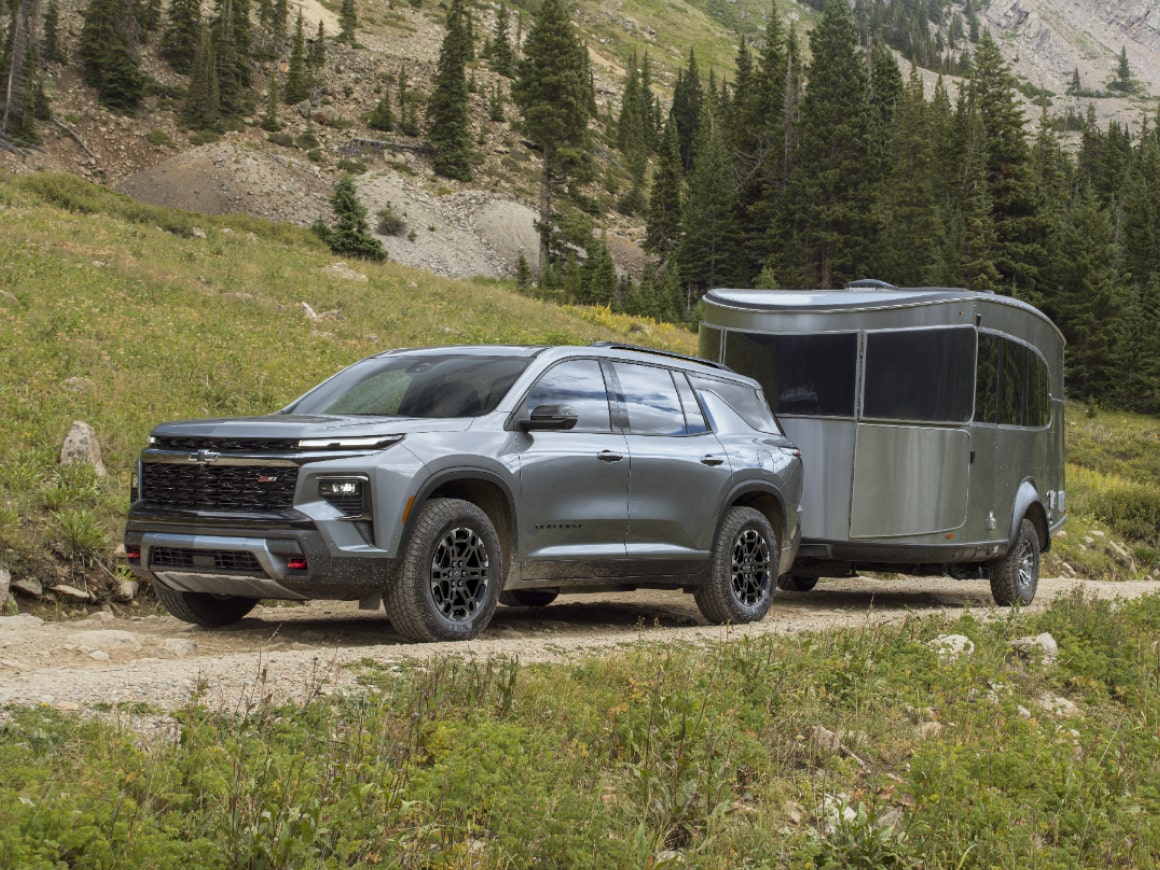 Une Chevrolet Traverse 2027 remorquant une remorque sur une route bordée d’arbres.