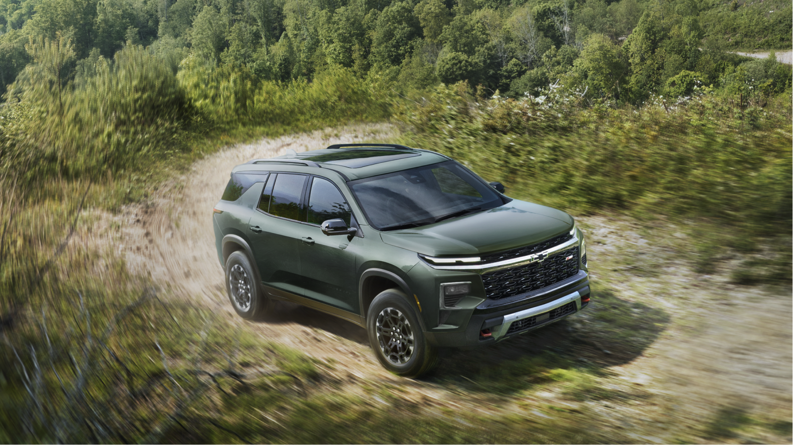 Une Chevrolet Traverse 2027 roulant seule sur une route bordée d’arbres.