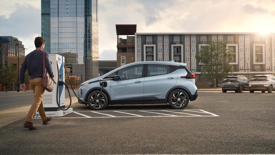 Une personne marche vers une Bolt EV 2023 branchée à une borne de recharge.