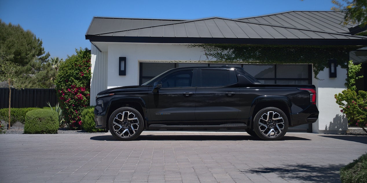 Side view of a 2025 Chevrolet Silverado EV next to a house surrounded by trees.