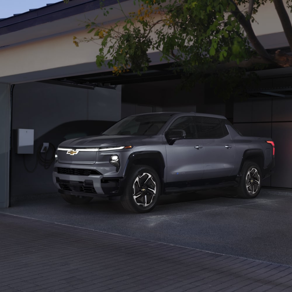 2026 Chevrolet Silverado EV Parked in a Garage Next to a Home Charging Station.