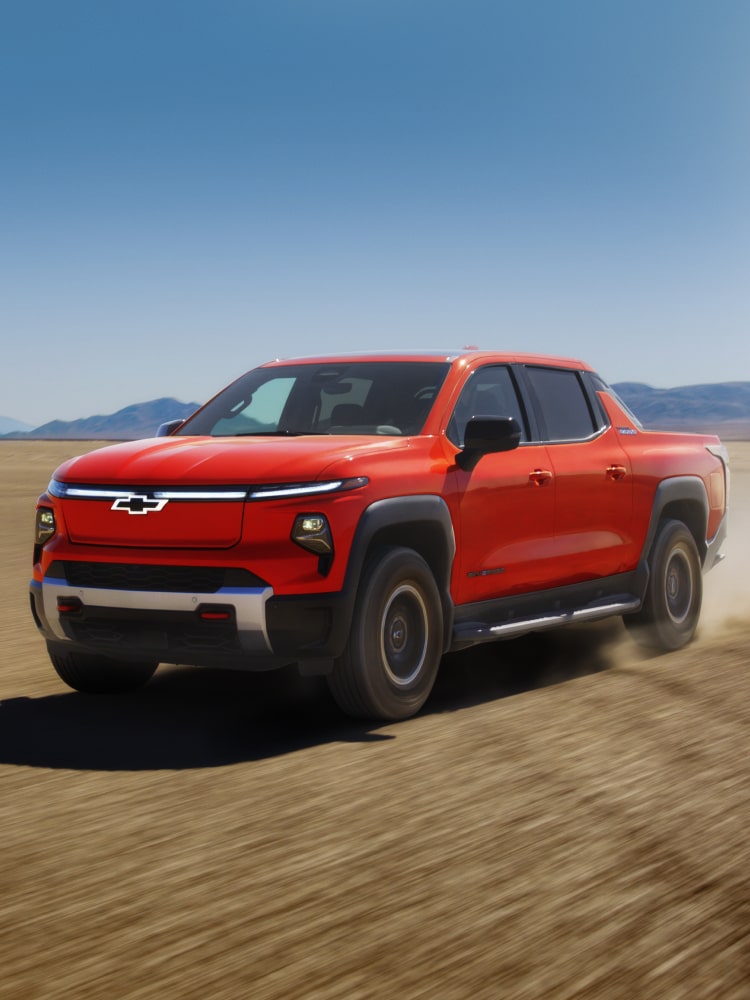 2026 Silverado EV Driving on a Dirt Terrain With Mountains in the Distance.