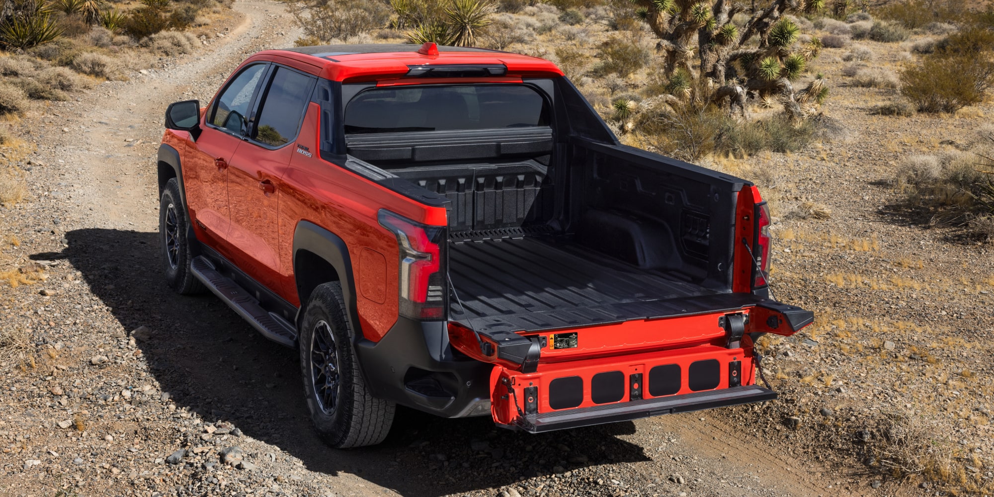 Back-side view of an the 2026 Chevrolet Silverado EV driving on a Rocky Road under a Sunny Day.
