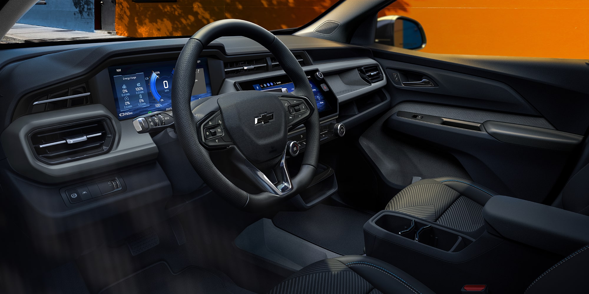 L’intérieur d’une Chevrolet Bolt EUV 2027, montrant un tableau de bord numérique à double écran et un système d’infodivertissement, avec un volant gainé de cuir noir et gris ainsi que des sièges assortis.